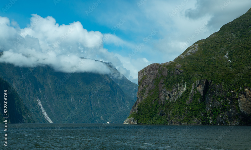 Rolling clouds coming over mountains and a waterfall in a fjord at Milford Sound New Zealand
