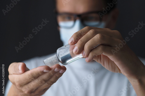 Man in medical mask using small transparent bottle sanitizer  alcohol gel. Selective focus.