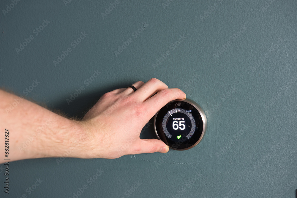 Fototapeta premium Green tech- Electric thermostat to save money and energy. Hand present to make adjustments.
