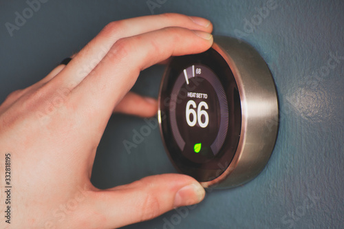 Hand operating smart thermostat to save money. Hand making adjustments by turning knob. Smart home.