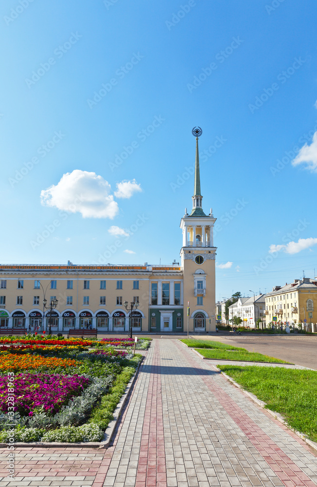 Siberian city of Angarsk. Citizens traditionally decorate the central square of the city with beautiful flower beds in the summer. View of the city clock tower with a spire