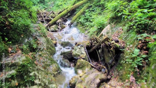 Medium wide angle Dolly in Drone shot of a small stream, rocks, and surrounding greenery in canyon hudicev greben during the day photo