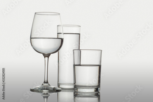 Vasos de cristal y copa con agua sobre una superficie y fondo blanco