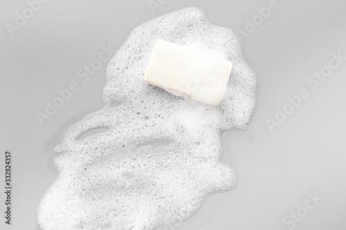 Soap bar with bubbles on grey background top-down
