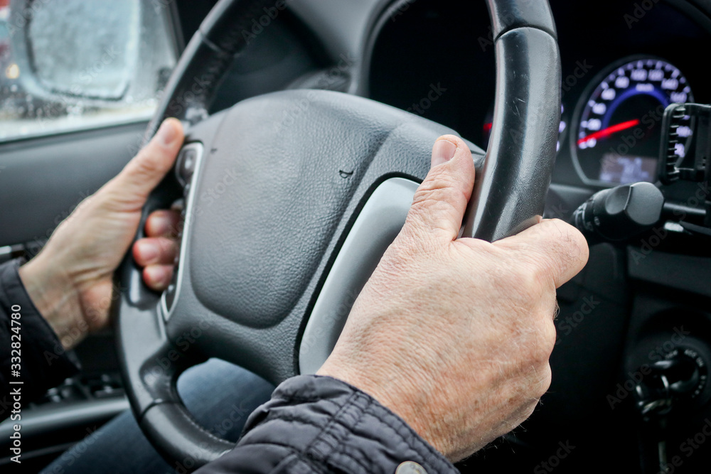 Naklejka premium Men's hands on the steering wheel of a car. The driver controls the car.