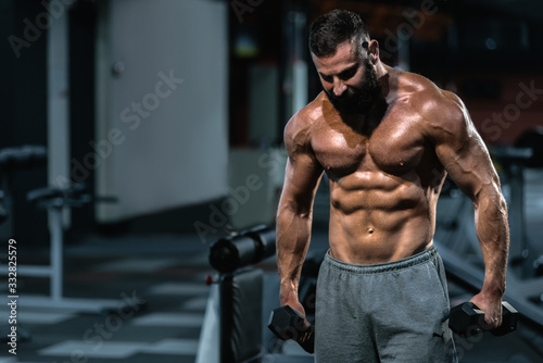 Portrait of strong handsome fit man exercising in gym with dumbbells