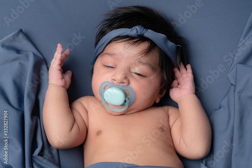 Half sleeping Newborn infant baby boy with pacifier on blue background