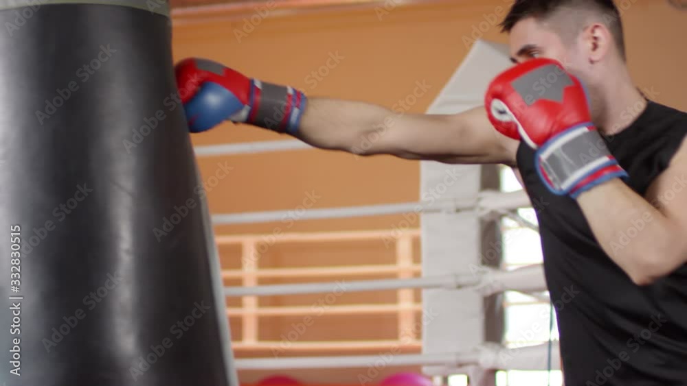 Handheld camera shot of caucasian male boxer in protective gloves hitting heavy bag while training in gym Handheld camera shot of caucasian male boxer in protective gloves hitting heavy bag while training in gym