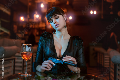 Sexy young woman sits at a table and holds a gun in her hands.