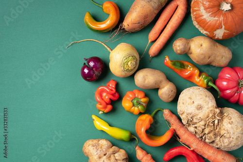 Trendy ugly organic vegetables. Assortment of fresh eggplant, onion, carrot, zucchini, potatoes, pumpkin, pepper in craft paper bag over green background. Top view. Cooking ugly food concept. Non gmo