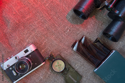 Binoculars, compass, camera lie on canvas. Film reel, negative film. Travel concept.