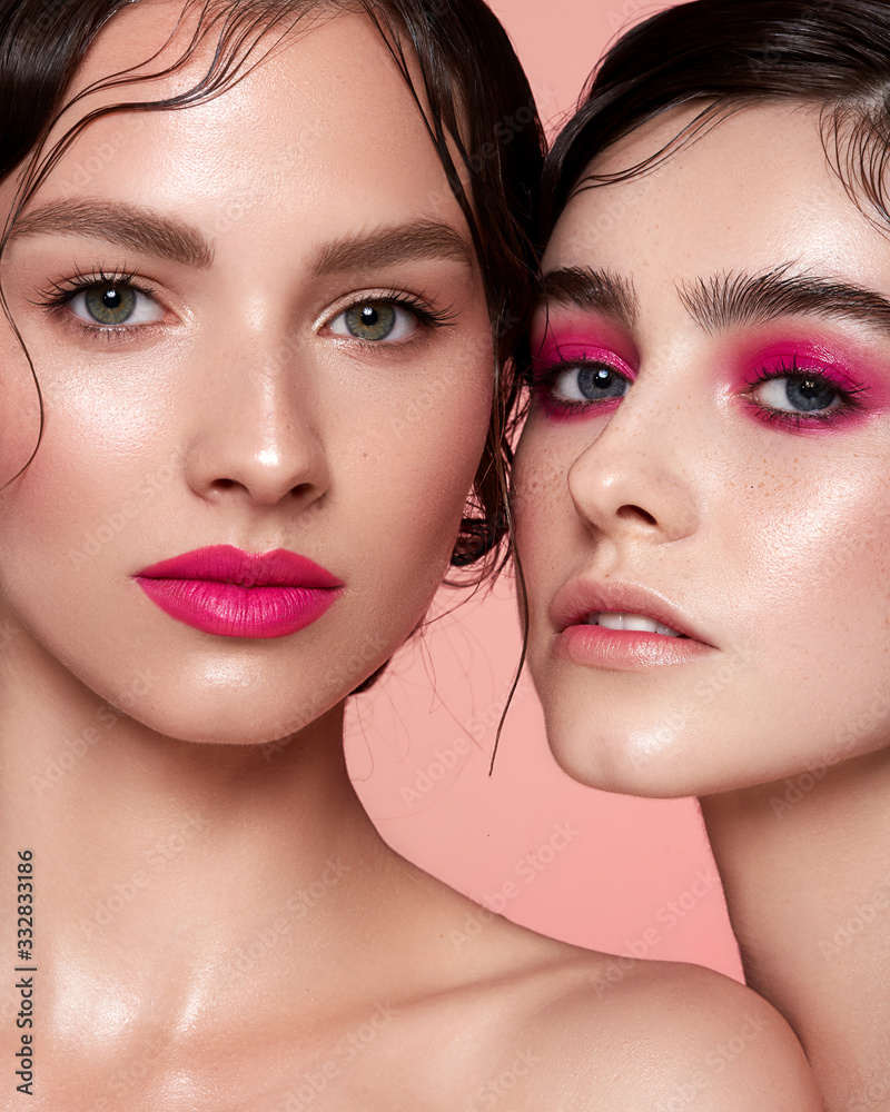 Two young girls on a pink background with pink make-up on lips and eyes. Clean skin. Natural retouching Two young girls on a pink background with pink make-up on lips and eyes. Clean skin. Natural retouching