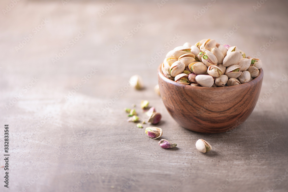 Green pistachio nuts in wooden bowl on wood textured background. Copy space. Superfood, vegan, vegetarian food concept. Macro of pistachio nut texture, selective focus. Healthy snack.