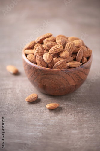 Almond nuts in wooden bowl on wood textured background. Copy space. Superfood, vegan, vegetarian food concept. Macro of almond nut texture, selective focus. Healthy snack photo