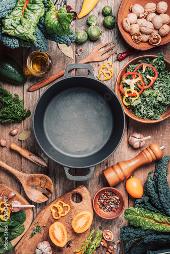 фотографія Various organic vegetables ingredients and empty iron cooking pot, wooden bowls, spoons on wooden background