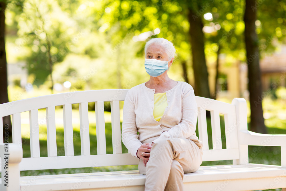 Fototapeta premium health, safety and pandemic concept - sad senior woman wearing protective medical mask for protection from virus sitting on bench at summer park