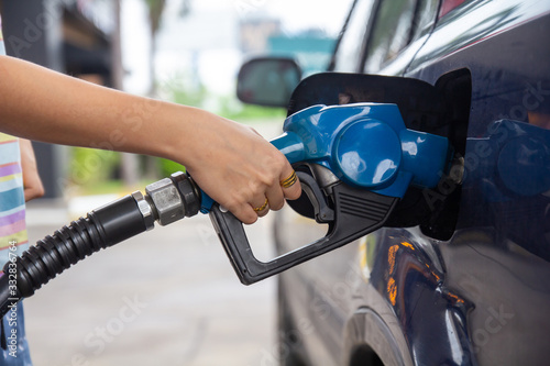 Blue car at gas station filled with fuel. Closeup woman hand pumping gasoline fuel in car at gas station.