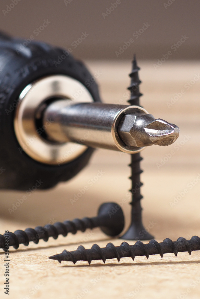 Crosshead screwdriver and screws lie on a sheet of fiberboard. Illustration on the topic of construction or repair of a house close-up. Vertical light shot in warm yellowish tones. Macro