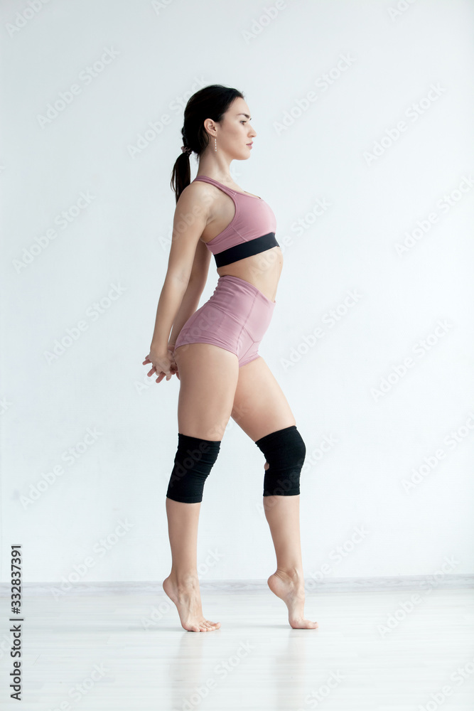 Sporty slim girl in pink sportswear stands straight holding hands behind her back warming up before workout