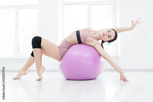 Young slender girl strengthens the back muscles with the help of fitness ball