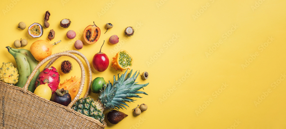 Exotic fruits in straw summer bag on yellow background. Top view. Copy space. Tropical fruits flat lay. Zero waste, plastic free concept. Travel and holiday concept. Vegan, vegetarian healthy diet