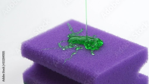 Super macro close up footage of purple sponge for dish and pouring detergent in form of green gel.