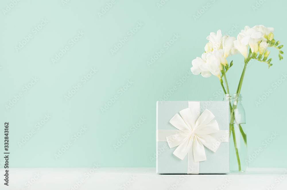 Beautiful fresh spring festive background with elegant standing gift box, white flowers in vase in green mint menthe interior on white wood board.