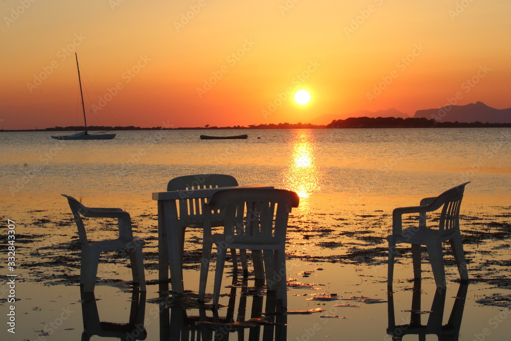tables and chairs by the sea at sunset which sets and boats moored