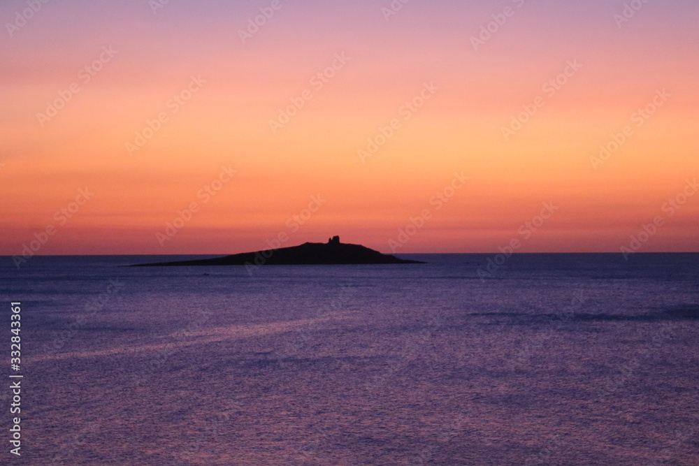 sunset over calm sea and an island in the background