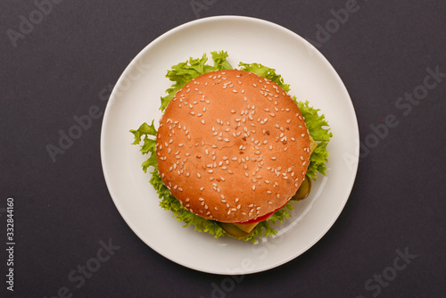Classic burger served on white plate over black background. Meat hamburger flat lay. Junk food, fast food concept.