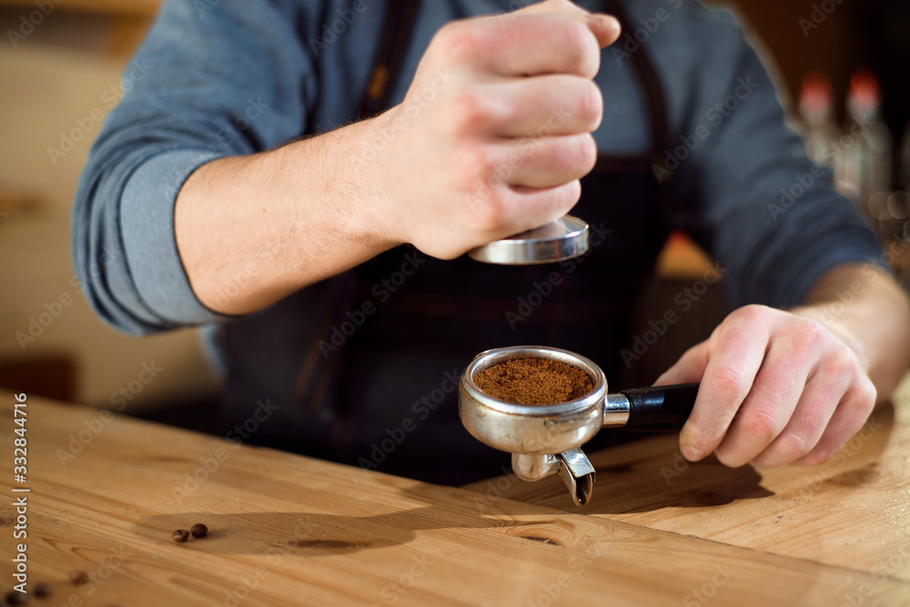 Barista presses ground coffee using tamper in a coffe shop