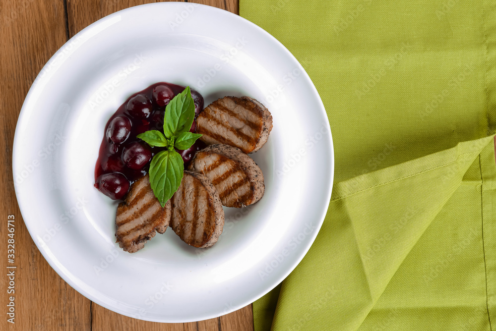 Grilled meat pieces with berry sauce served on a white plate over dark rustic wooden background. Italian cuisine. Grilled meat pieces with berry sauce served on a white plate over dark rustic wooden background. Italian cuisine.
