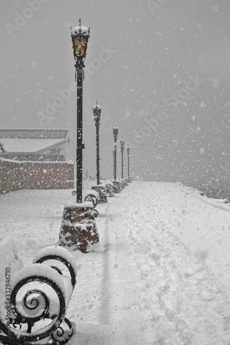 Snowfall on the city embankment benches and lanterns