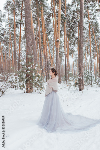 a beautiful girl in a wedding dress stands in a winter pine forest