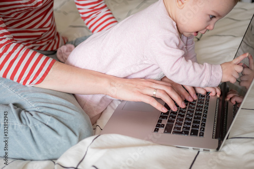 Mother working on laptop at home together with infant baby. Distance work, education. work from home, working mother.