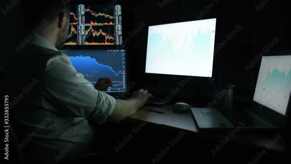 Stockbroker in white shirt is working in a dark monitoring room with display screens. Stock Exchange Trading Forex Finance Graphic Concept. Businessmen trading stocks online. Stockbroker in white shirt is working in a dark monitoring room with display screens. Stock Exchange Trading Forex Finance Graphic Concept. Businessmen trading stocks online.