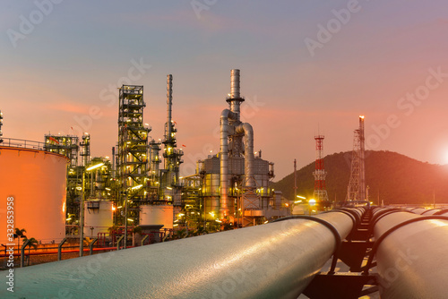 Fotografie Oil refinery plant near oil tanker storage or power plant with pipe line trasport on sunset, twilight bacckground