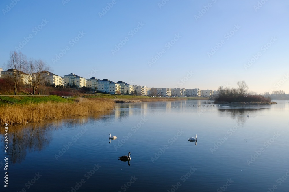 An estate of identical apartment blocks on the lake and its reflection in water, on the outskirts of the city. Idyllic view with blue sky and blue water. Gdansk South, Zakoniczyn, Poland An estate of identical apartment blocks on the lake and its reflection in water, on the outskirts of the city. Idyllic view with blue sky and blue water. Gdansk South, Zakoniczyn, Poland