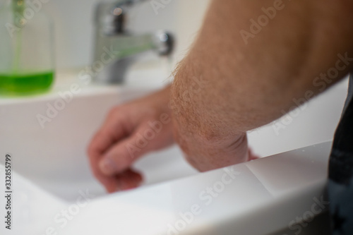 Blurred picture of a man who  is wahing his hands at the white sink in the bathroom.
