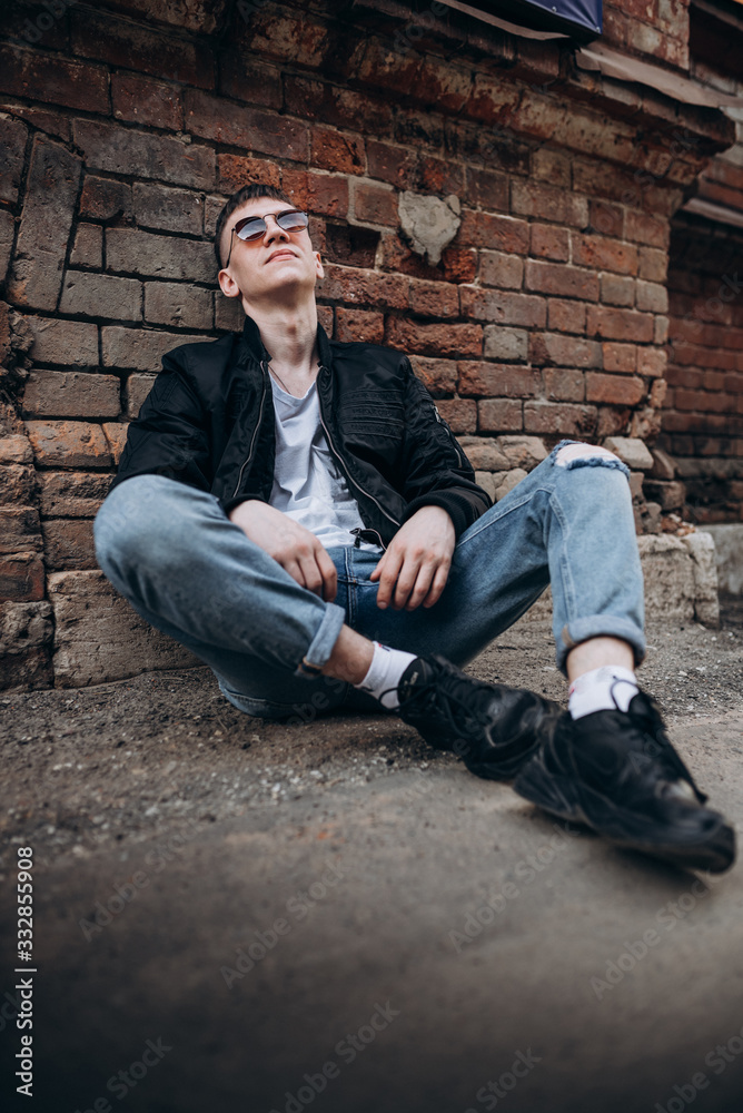 a young guy in dark glasses, a black jacket, a white t-shirt and blue jeans walks along the street a young guy in dark glasses, a black jacket, a white t-shirt and blue jeans walks along the street