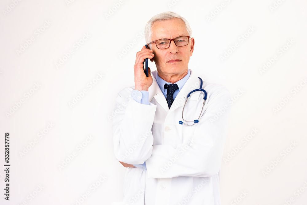 Senior male doctor using mobile phone while standing at isolated white background Senior male doctor using mobile phone while standing at isolated white background
