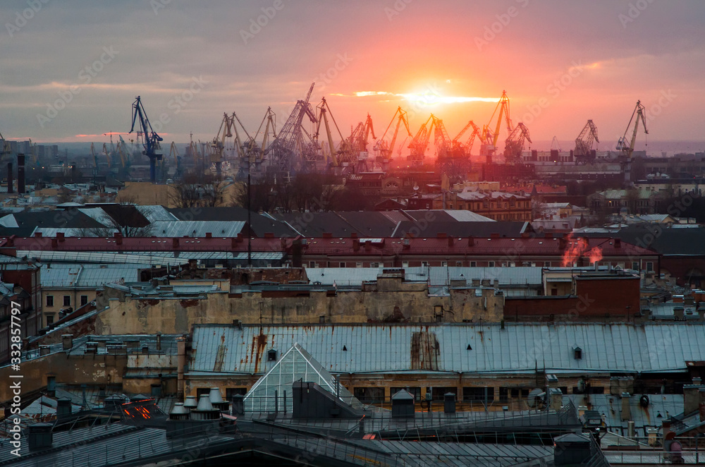 Sunset on the background of roofs of houses and cranes