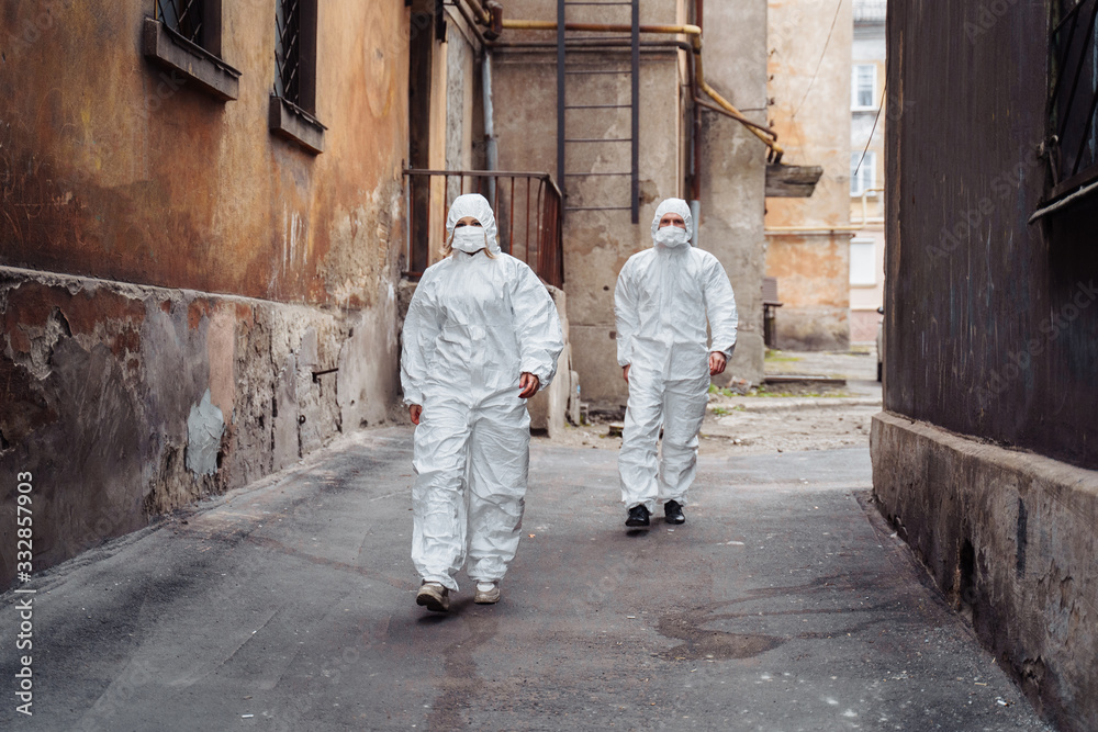 People with protective suits and respirators walking outdoors along deserted, abandoned, ruined street. Coronavirus concept. People with protective suits and respirators walking outdoors along deserted, abandoned, ruined street. Coronavirus concept.