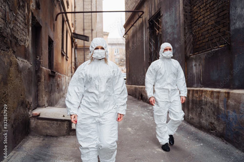 People with protective suits and respirators walking outdoors along deserted, abandoned, ruined street. Coronavirus concept.