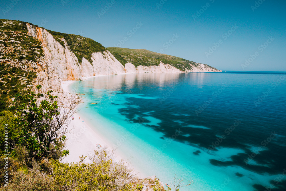 Fototapeta premium Holiday vacation. Fteri beach, Kefalonia, Greece. Calm clear blue emerald green turquoise sea with dark deep pattern and rocky coastline in background