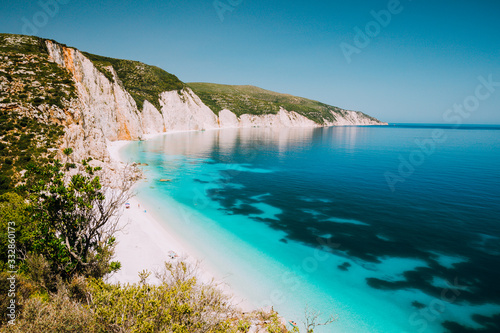 Holiday vacation. Fteri beach, Kefalonia, Greece. Calm clear blue emerald green turquoise sea with dark deep pattern and rocky coastline in background