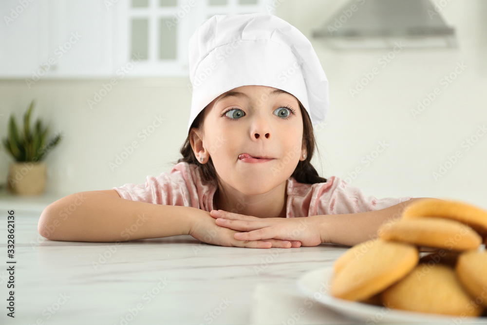 Cute little girl wearing chef hat at table in kitchen Cute little girl wearing chef hat at table in kitchen