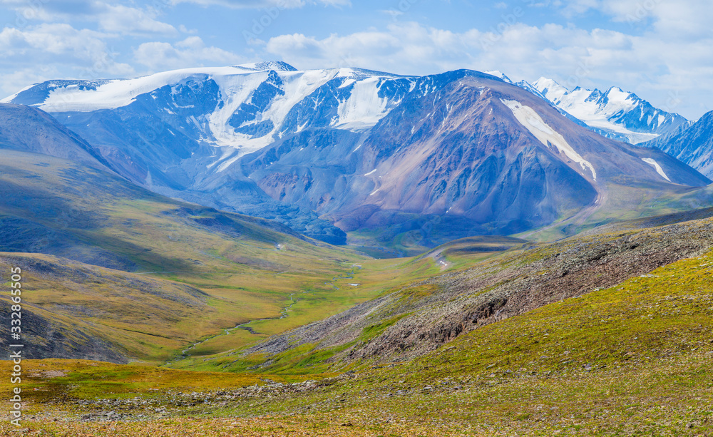 View of a mountain valley. Tundra, treeless mountain slopes, snow-capped peaks.