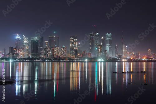 Night View of Mumbai's ever growing city skyline full of tall buildings casting colorful reflections on the sea. Shot taken from tourist attraction near Bandra Reclamation. Mumbai, Maharashtra, India.