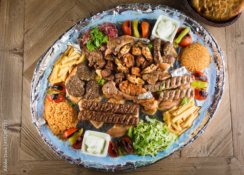 Full view of Persian Mix Kebab of minced meat and chicken With Rice and french fries and vegetables in a large traditional tray on wooden table